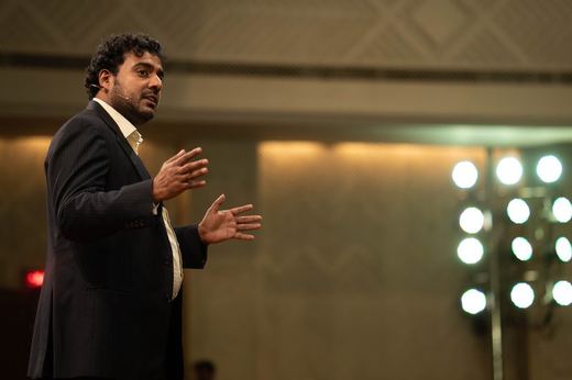 Antano speaking on stage under the house lights